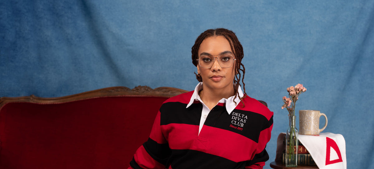 Model in a red and black striped rugby shirt seated on a red velvet sofa beside a Delta Sigma Theta scarf